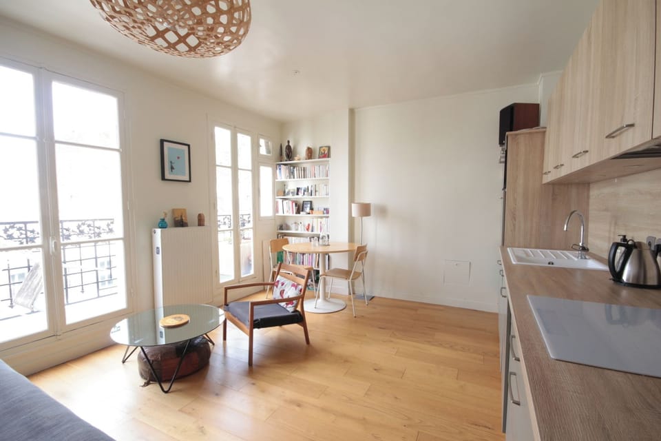 Séjour baigné de lumière avec grandes fenêtres, parquet et bibliothèque — appartement Paris 19 près du Canal / Sun-filled living room with large windows, hardwood floor and bookshelves — apartment in Paris 19 near the Canal