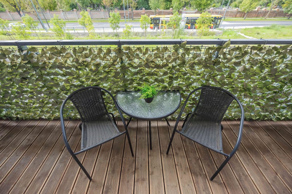 A cozy balcony furnished with a round table and two chairs. Greenery along the railing adds privacy and creates a relaxing outdoor setting.