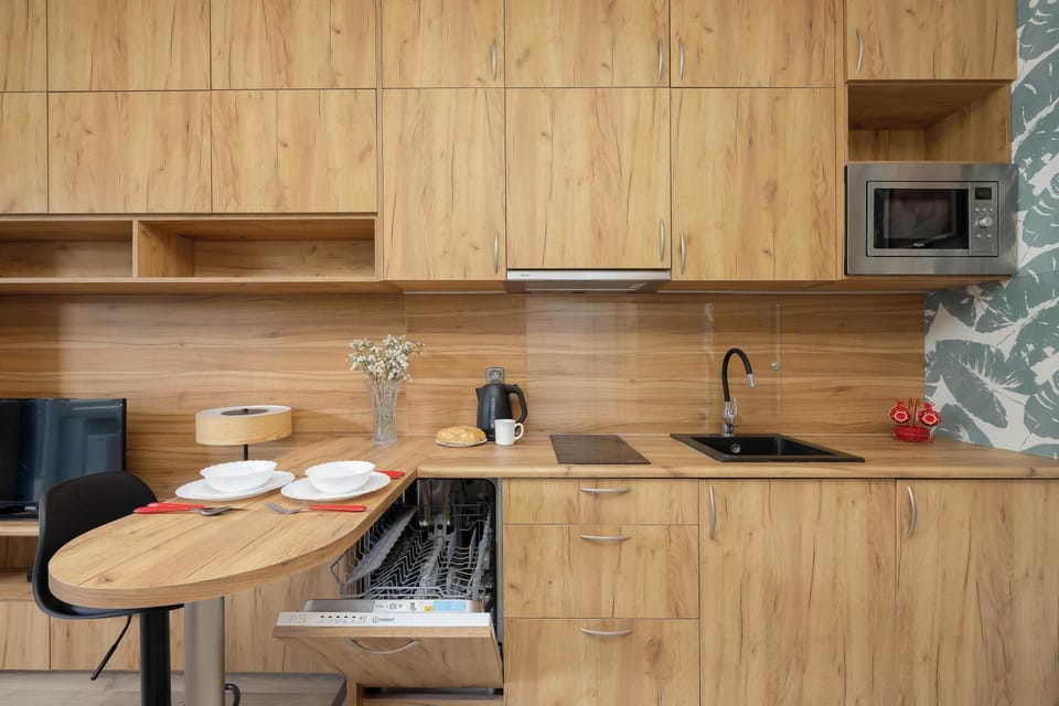 A close-up view of the kitchenette with wooden cabinets, a microwave, and a countertop. The dining table and two stools are positioned directly beside the cooking area.