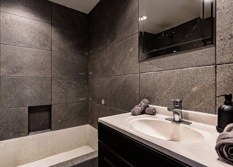 Dark gray tile surrounds a clean vanity in this modern bathroom.