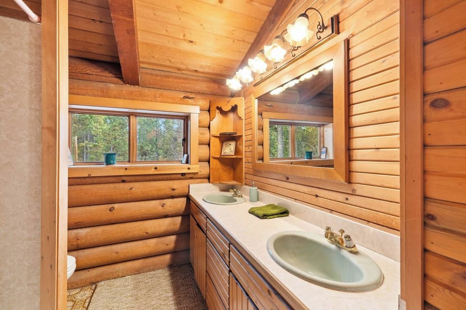 Rustic double-vanity bathroom with warm wood finishes and forest views