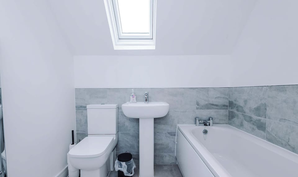 A bright modern bathroom features a clean white bathtub with grey tiled trim and a separate glass-door walk-in shower enclosure.