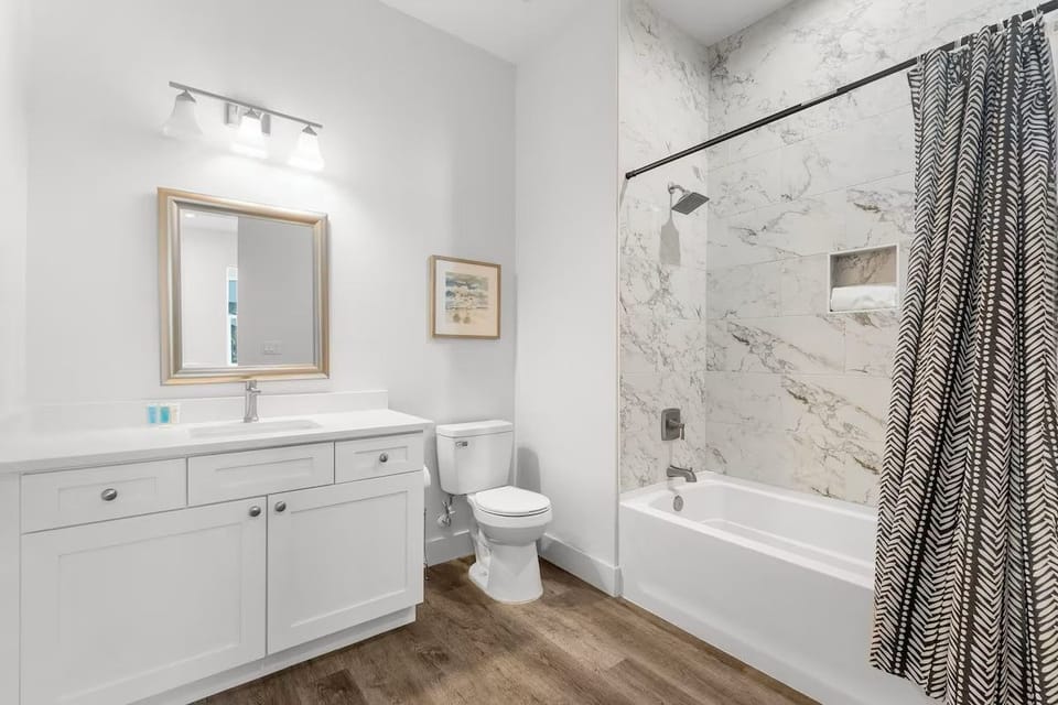Refresh and rejuvenate in this pristine bathroom featuring a clean modern vanity with a large mirror and a combination tub and shower with stylish tile finishes.