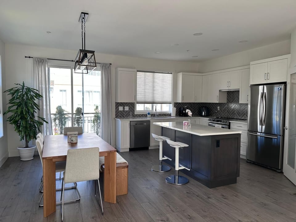 Dining area with wooden table, beige chairs, and a black pendant light next to sliding glass doors.