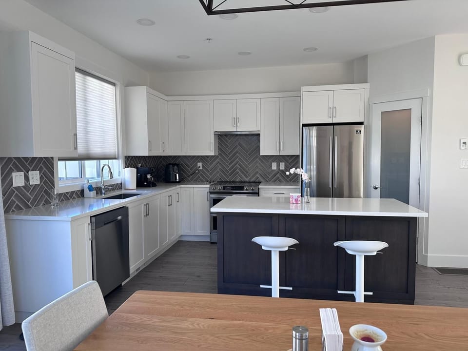 White shaker cabinets and dark wood island with quartz countertops in the kitchen, framed by gray herringbone tile backsplash.