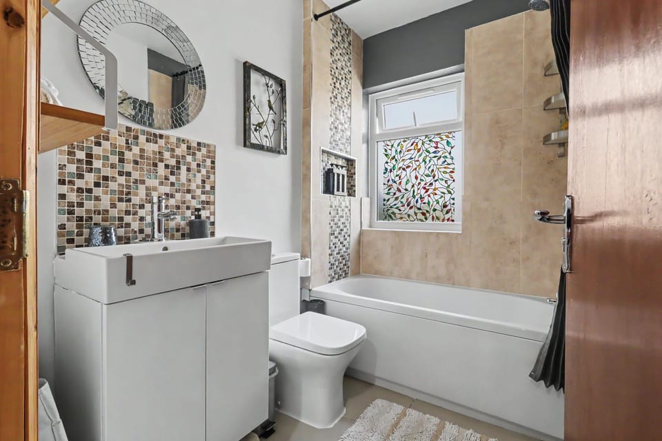 Stylish modern bathroom with full tub, mosaic accents, and privacy window