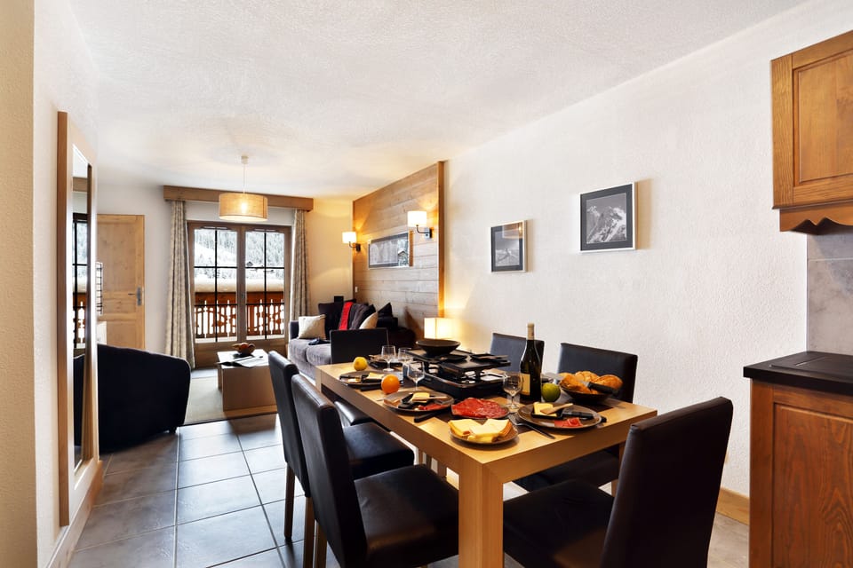 A raclette set and Savoyard charcuterie cover the dining table, seating six beneath black-and-white mountain prints.