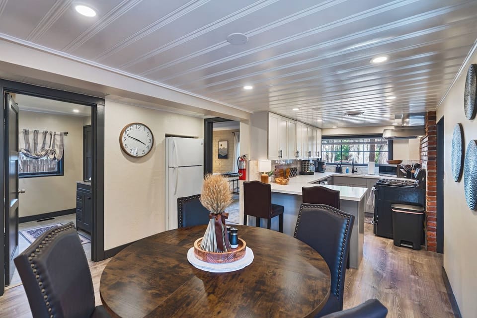 A round wood dining table with nailhead-trim chairs opens straight into the renovated kitchen just beyond. Warm, connected, and effortlessly functional, it`s an easy setup for shared meals together.