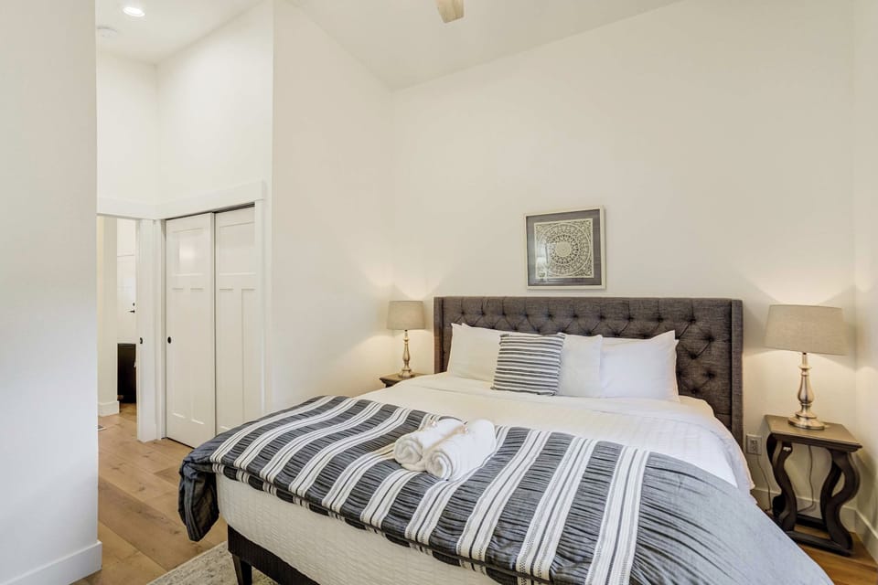 A deep charcoal headboard anchors the bed, layered with a striped throw across crisp white bedding, with closet doors along the wall to one side. Lamps on either side make it easy to read late without waking anyone across the hall.