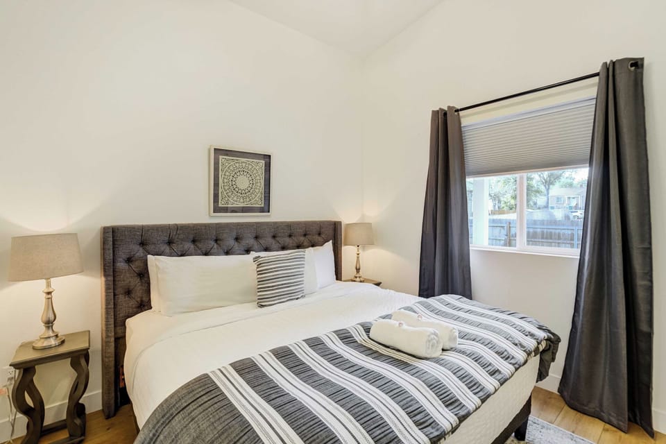 Floor length curtains frame the window in this bedroom, drawing closed for a dark room when mornings are meant to start slowly. The bed sits centered between two lamps, with open floor on either side to move around freely.