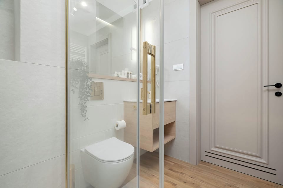 A modern bathroom with a glass-enclosed shower and a wall-mounted toilet. The light interior is finished with simple, elegant details.