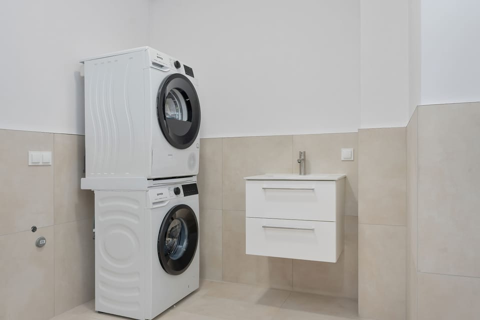A shared laundry area with washing machines and tumble dryers stacked against the wall. The facilities provide convenient access to laundry and drying facilities within the building.