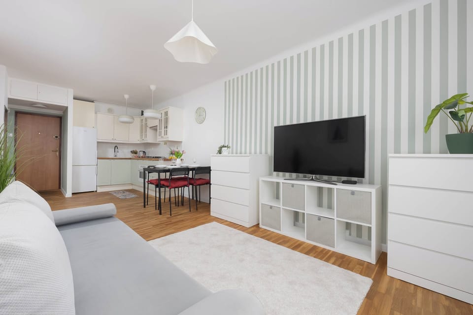 A living room corner focused on a television mounted above a low-profile white cabinet. Striped walls add texture to the neutral color palette of the room.