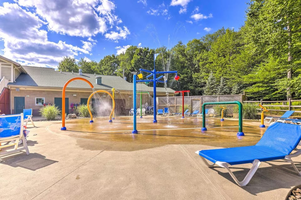 An outdoor splash pad features colorful water sprayers and surrounding lounge seating.