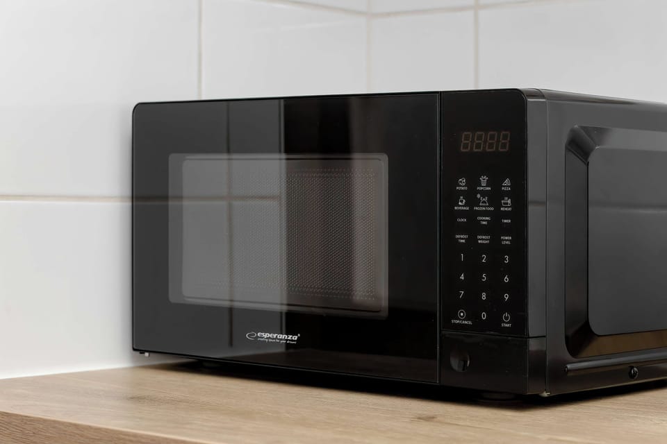 A sleek black microwave is positioned on a wooden kitchen countertop. It stands out against the plain white wall behind it.