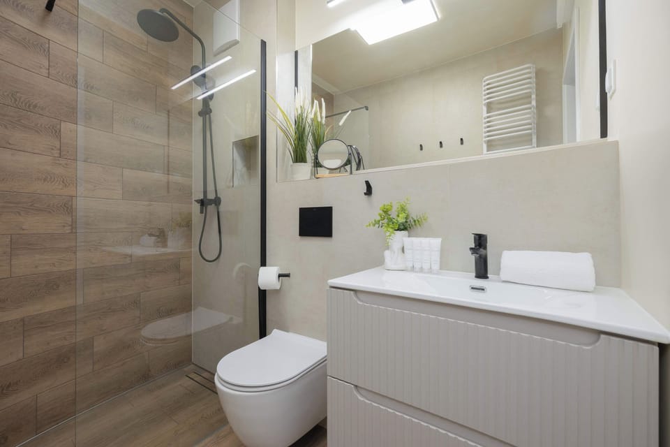 A modern bathroom interior features a walk-in glass shower and light beige tiling on the walls. A sleek white vanity with a rectangular sink provides a clean and contemporary look.