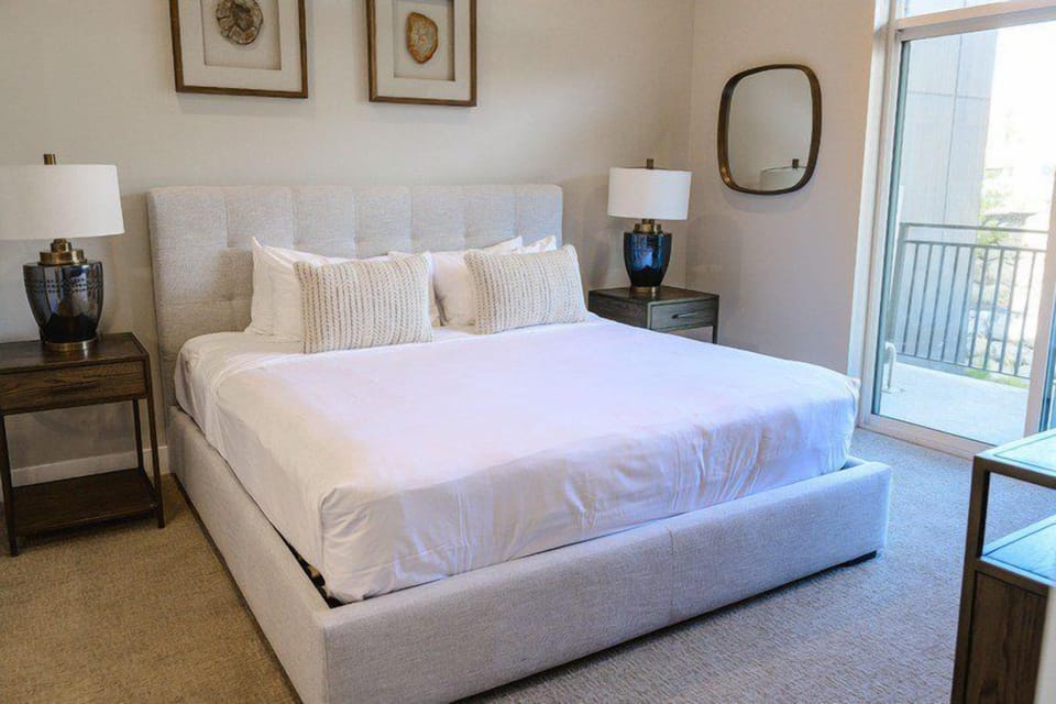 King bed with tufted linen headboard, dual nightstands, and balcony access