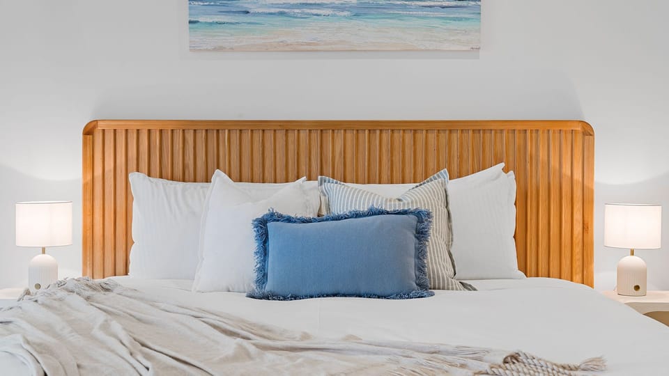 Comfortable bedroom featuring a wooden headboard, crisp white linens, and a blue accent pillow.