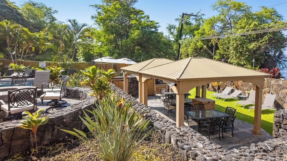 A lush tropical oasis awaits in this beautifully landscaped outdoor space, where covered pavilions and bright loungers offer multiple spots to relax under swaying palms and sunny skies.