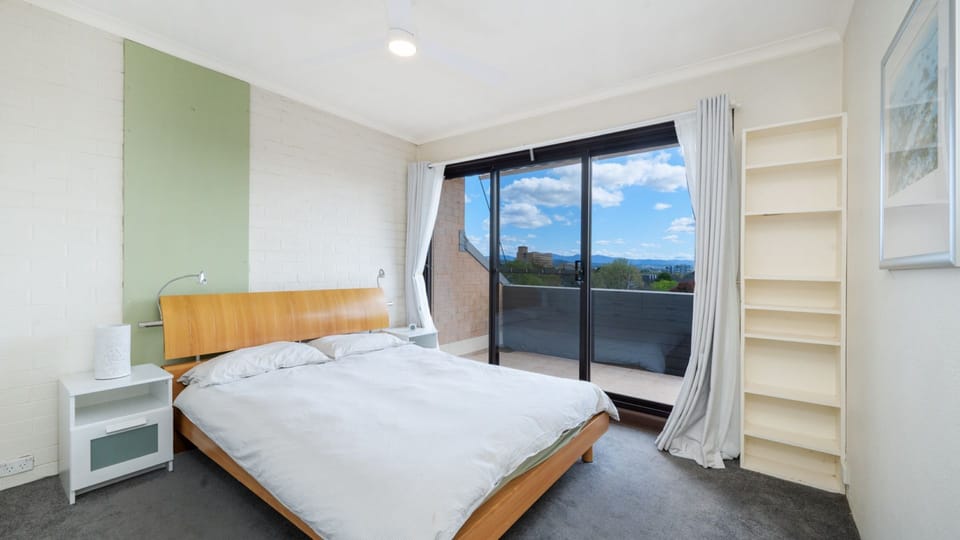 Spacious bedroom featuring a neatly made bed, bedside table, and large windows framing scenic outdoor views.