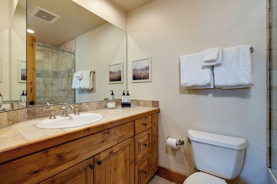 Step into your beautifully appointed bathroom, where warm wood cabinetry and stone countertops create a welcoming retreat. Fresh towels await, and a spacious walk-in shower promises a refreshing start to each day.