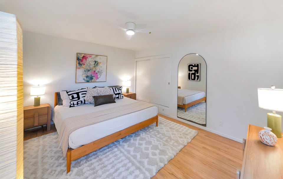 Bright, stylish bedroom with plush rug, warm lighting, and full-length mirror