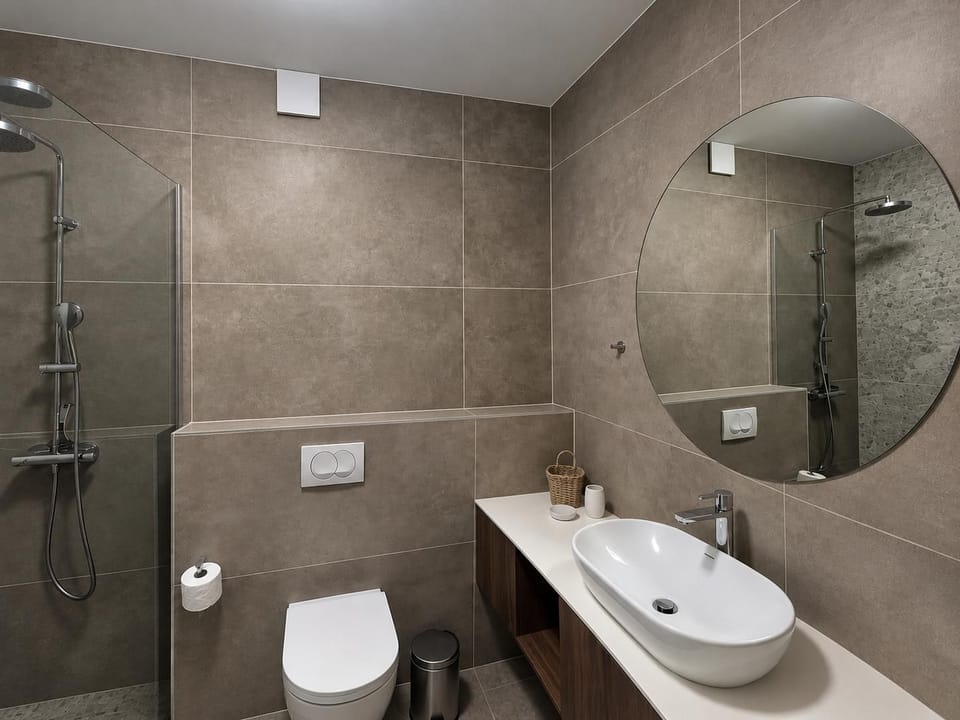 Modern bathroom with a sleek vanity, round mirror, toilet, and elegant stone-effect tiled finishes.