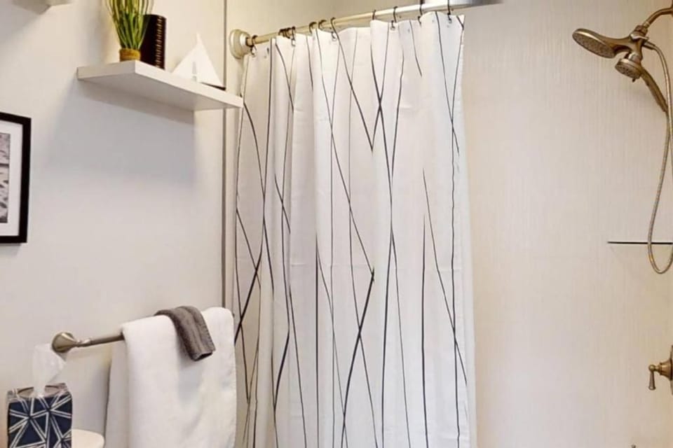 Antique bronze fixtures add a touch of warmth to this clean bathroom, where minimalist patterns and fresh linens create a calm space. A floating shelf and lush greenery provide a spa-like feel for your daily routine.