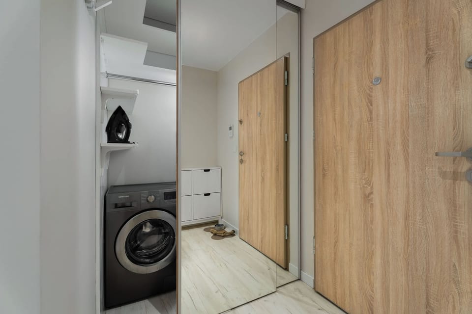 A modern bathroom featuring a washing machine. Light-colored tiles and natural wood finishes create a clean and contemporary interior.