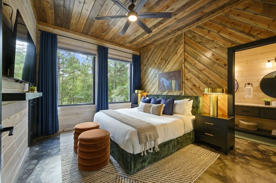Bedroom 1: king bed, private bath, TV, and big windows looking into the trees.