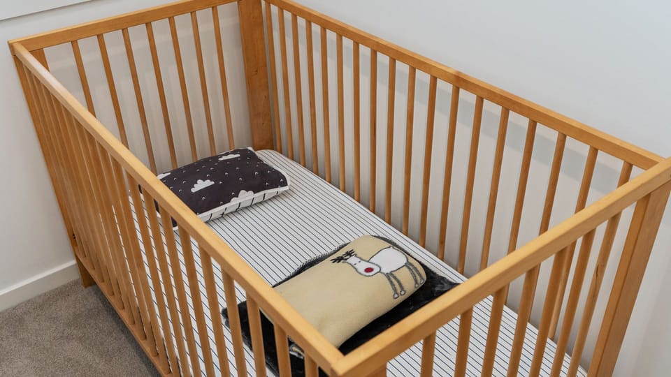 Nursery room featuring a wooden baby cot set with a mattress and bedding.   