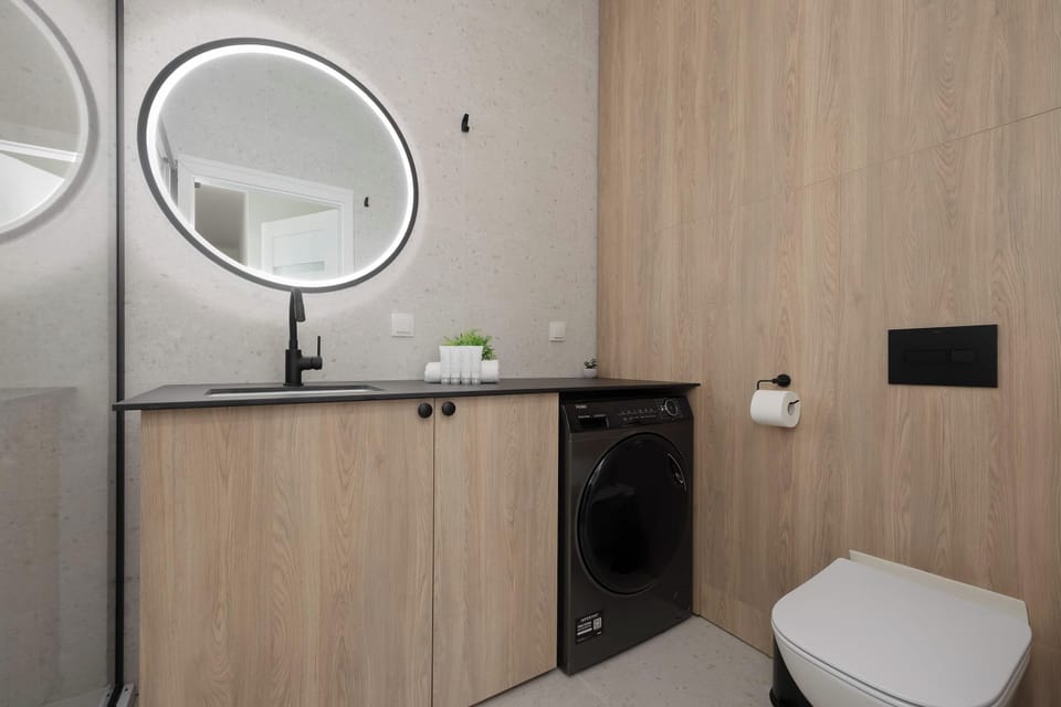 Modern bathroom with wooden vanity unit, round mirror, washing machine and toilet.