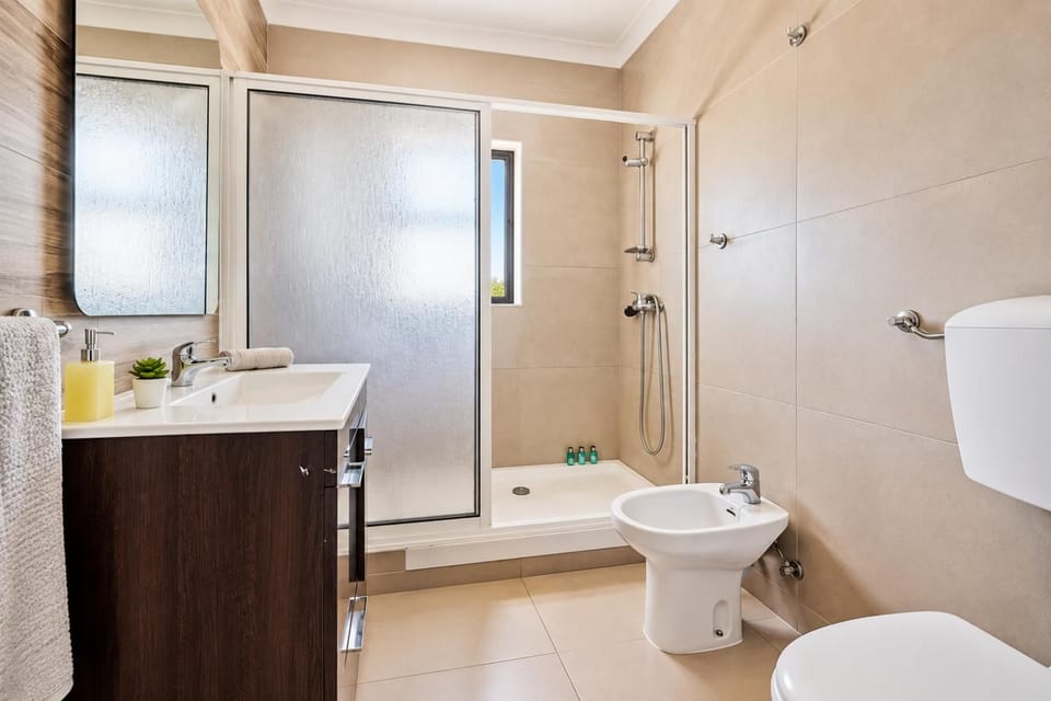 Modern bathroom with bathtub and shower, vanity unit, toilet, and clean neutral tiled finishes.