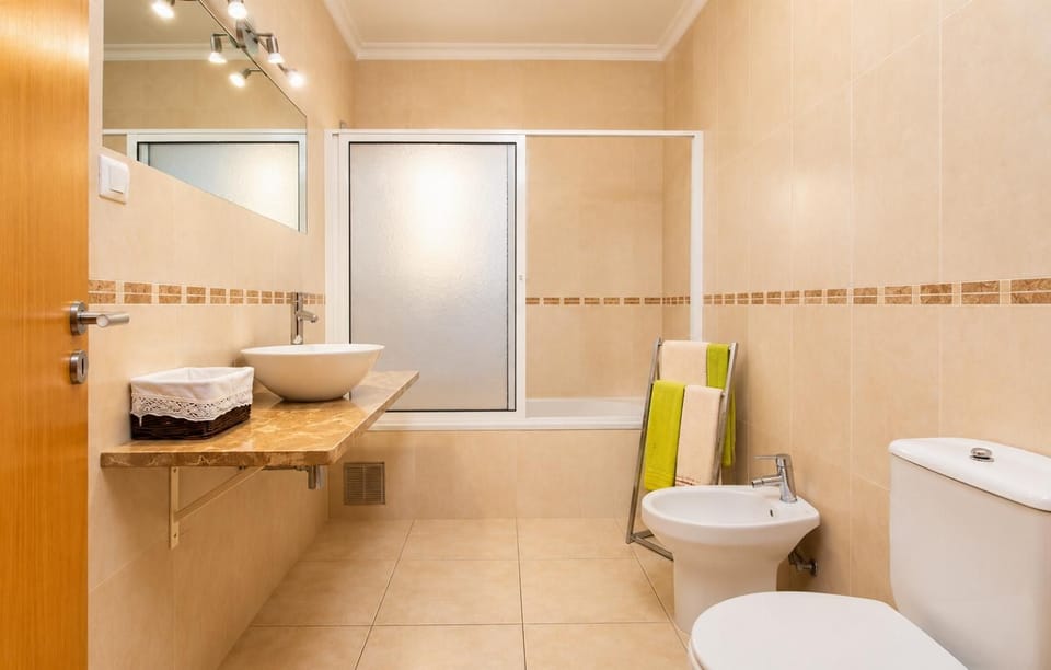 Spacious bathroom with a glass-enclosed shower, vanity basin, toilet, and bright contemporary tiled interiors.