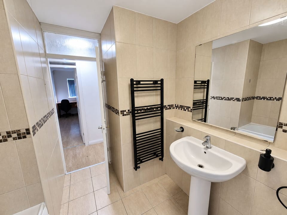 Bathroom: Spacious ensuite featuring cream tiling with decorative mosaic border, dual sinks, a black heated towel rail, 