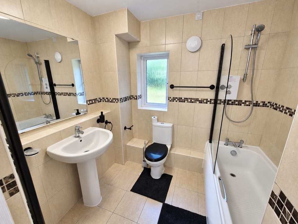 Bathroom: Contemporary space with cream-coloured tiles, white pedestal sink with curved mirror, white toilet with black 