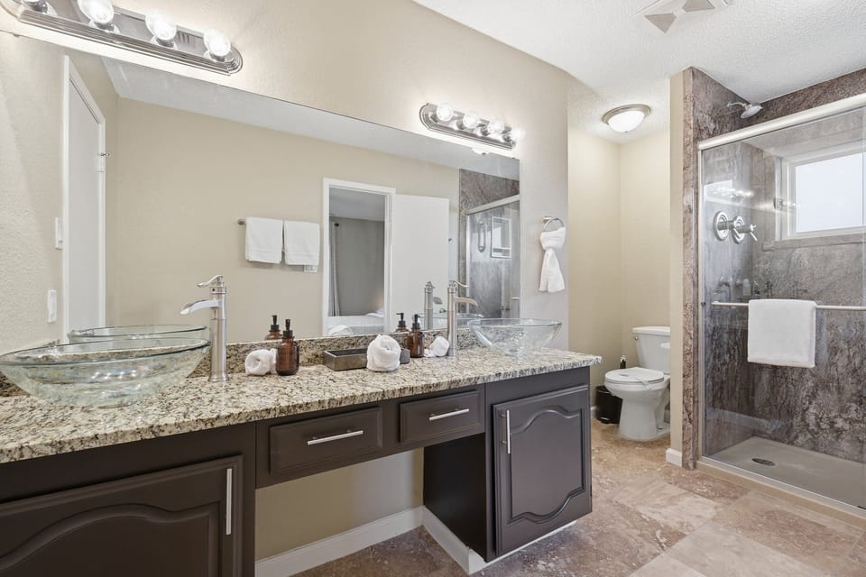 Primary en-suite bath with dual vessel sinks, granite counter, and tile shower.