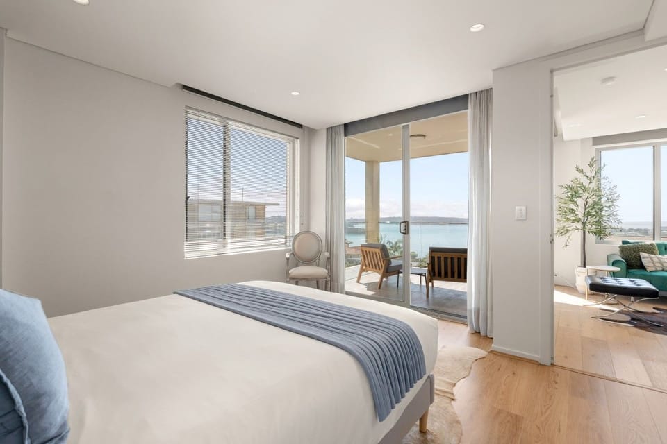 Bedroom with a queen bed, timber flooring and direct access to a private terrace with harbour views