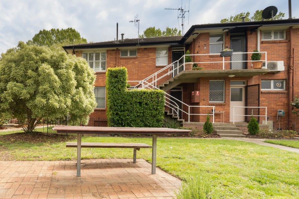 A lovely outdoor setting with established trees, green lawns and a simple bench, providing a peaceful spot to sit back and enjoy the surroundings.