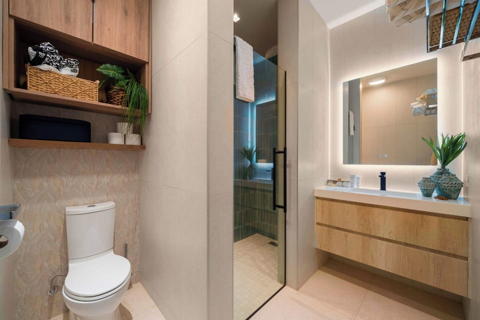 A bright, modern bathroom with warm wood cabinetry, an illuminated mirror, and a glass-enclosed walk-in shower.