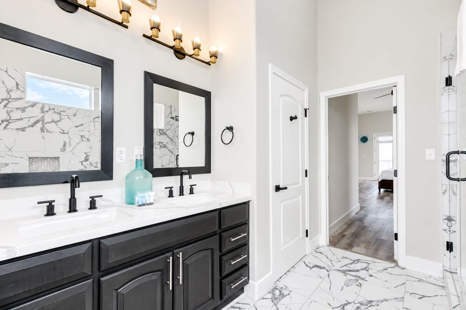 Bright full bathroom with a tub/shower combination, vanity storage, marble-look tile, and modern black fixtures.