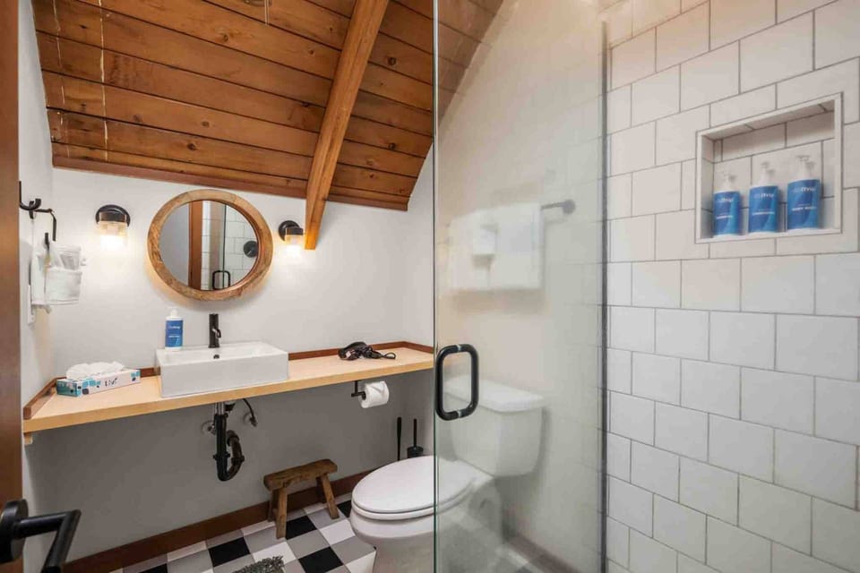 Modern bathroom featuring a vessel sink on a long wooden vanity, a round mirror, buffalo check flooring, and a subway-tiled walk-in shower.