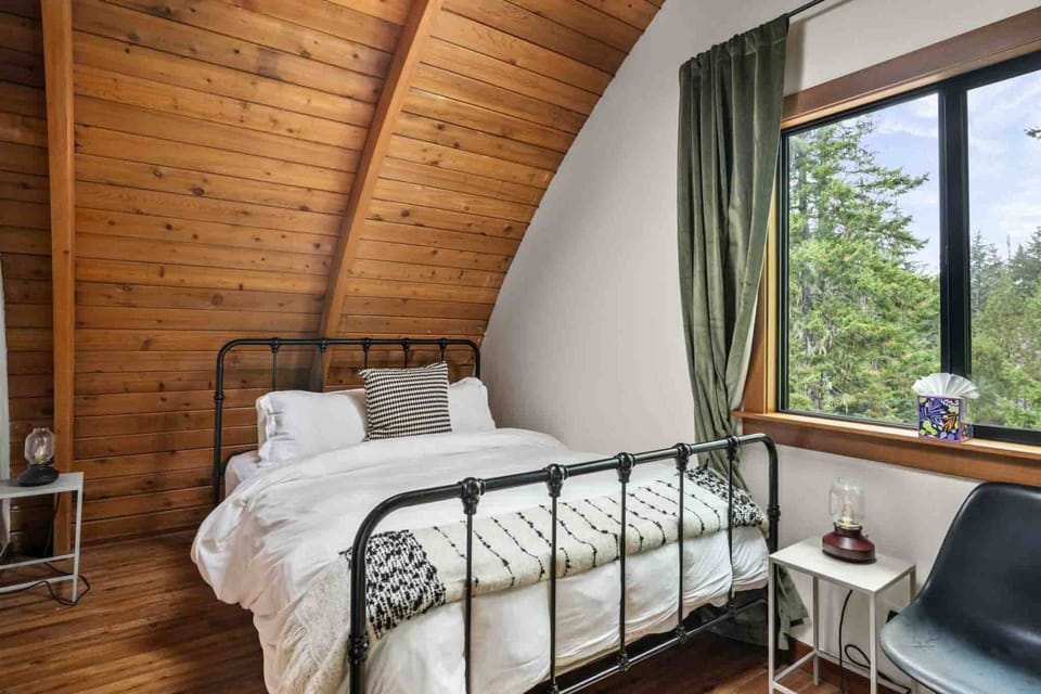Charming bedroom featuring a black metal bed frame set against sloped wood-paneled walls.