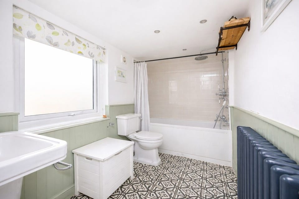 A bright, airy bathroom blending classic English style with modern comfort. Soft green tones and Georgian-inspired detailing are paired with a contemporary bath and shower over, creating a practical, spacious room that feels both timeless and fresh.