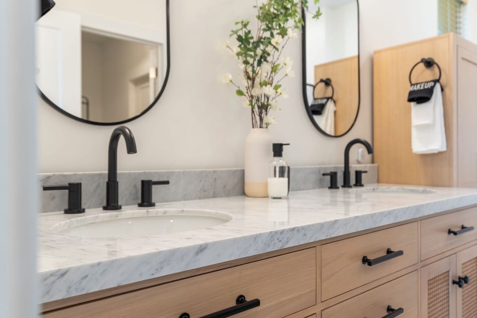 Freshen up in your spa-inspired bathroom, where dual marble vanities, sleek black fixtures, and modern round mirrors create a sophisticated retreat for your morning routine.