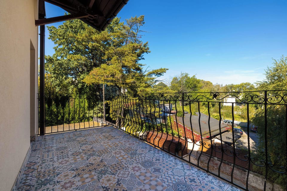 A spacious outdoor balcony with a tiled floor, a metal railing, and views of surrounding greenery and buildings. The area provides a pleasant spot to enjoy the outdoors.