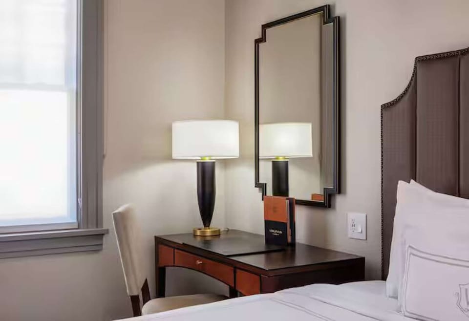 Desk with mirror, lamp, chair, and book beside bed frame