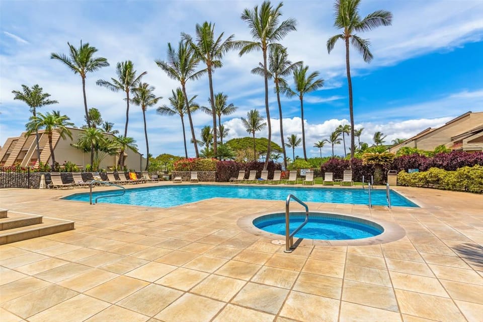 Resort swimming pool and circular spa surrounded by tiled decking, palm trees, and poolside lounge chairs.