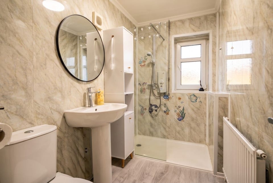 Walk-in shower with a pedestal basin and tall storage cabinet.