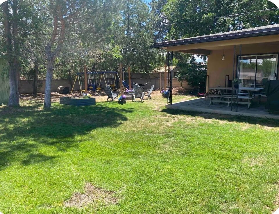 Grassy backyard with a covered patio, fire pit, and playset.